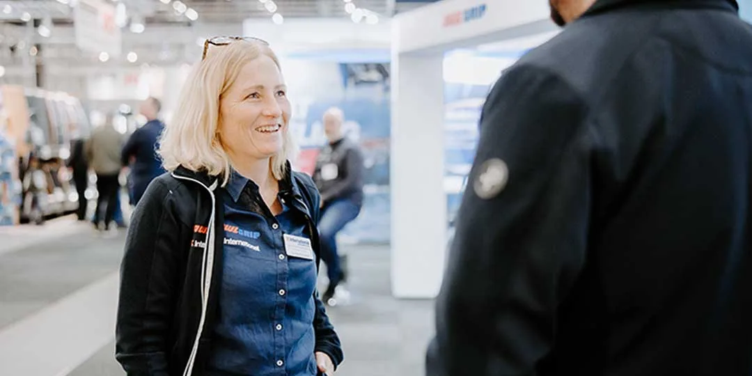 Leende kvinna i blå skjorta samtalar i en mässmonter.