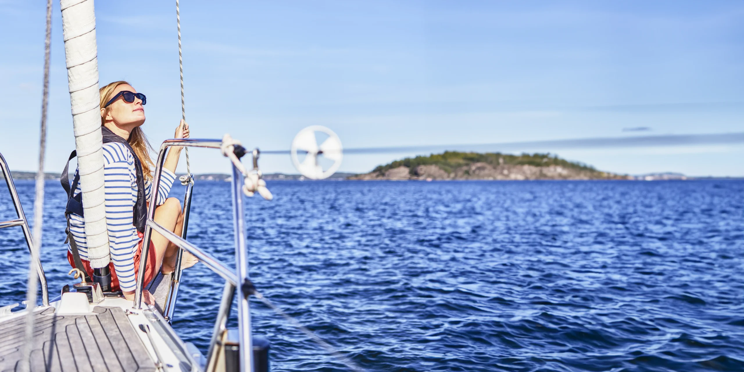 AFS_puff_startsida Ung kvinna seglar en vit segelbåt på lugnt vatten under klar himmel.