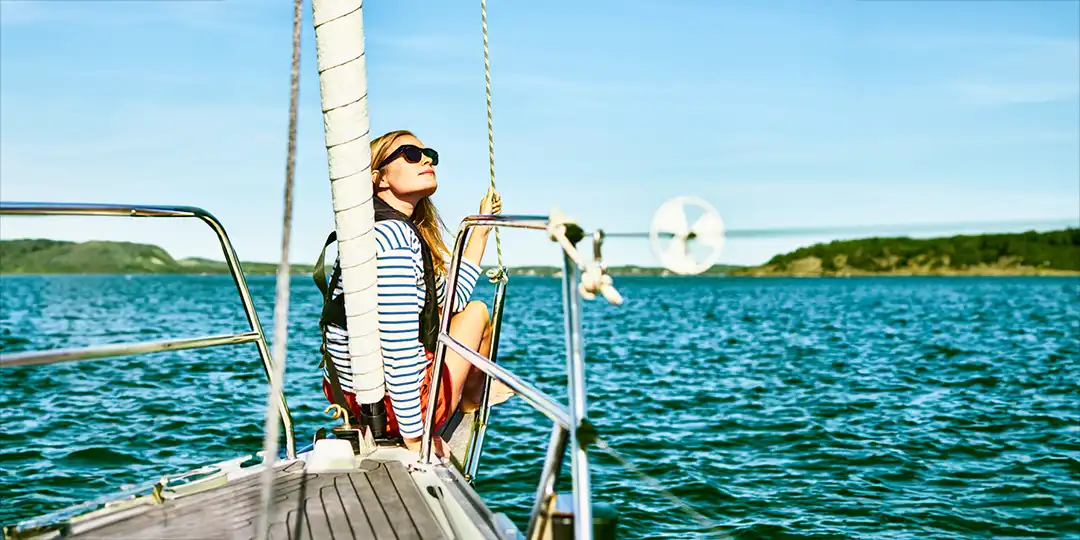puff start For visitors: Young woman sailing a white sailboat on calm water under a clear sky.