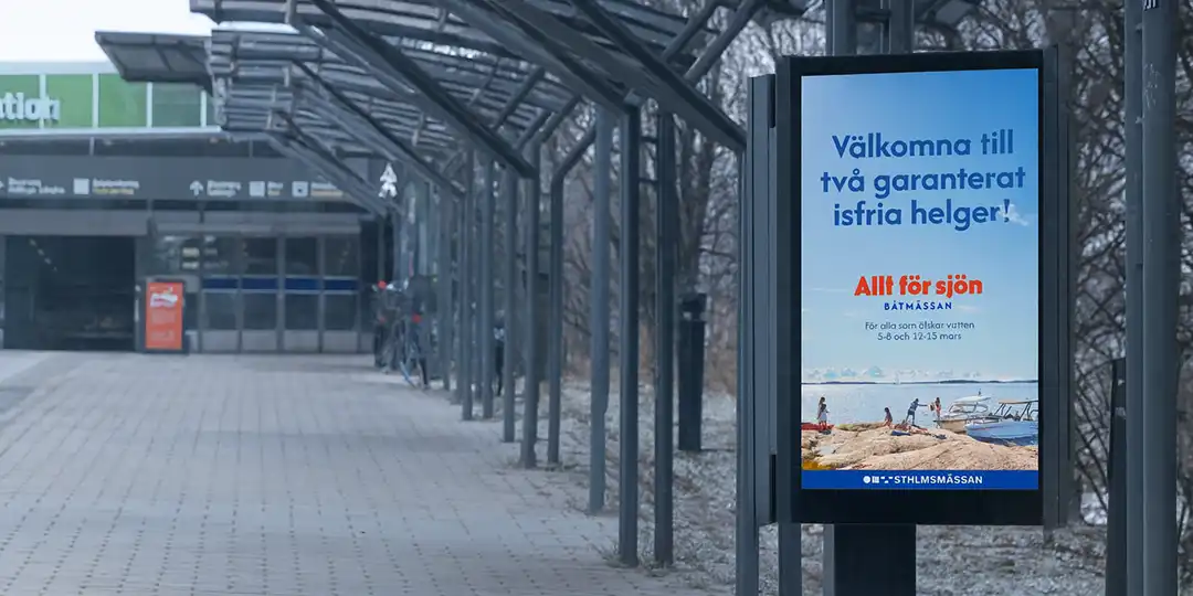 Digital skylt AFS kopiera Digital reklamskylt utomhus vid en gångväg med cykelställ och tak. Skylten visar en annons för Båtmässan Allt för sjön med texten ”Välkomna till två garanterat isfria helger! Allt för sjön, Båtmässan, 8–10 och 12–15 mars, Stockholmsmässan”.
